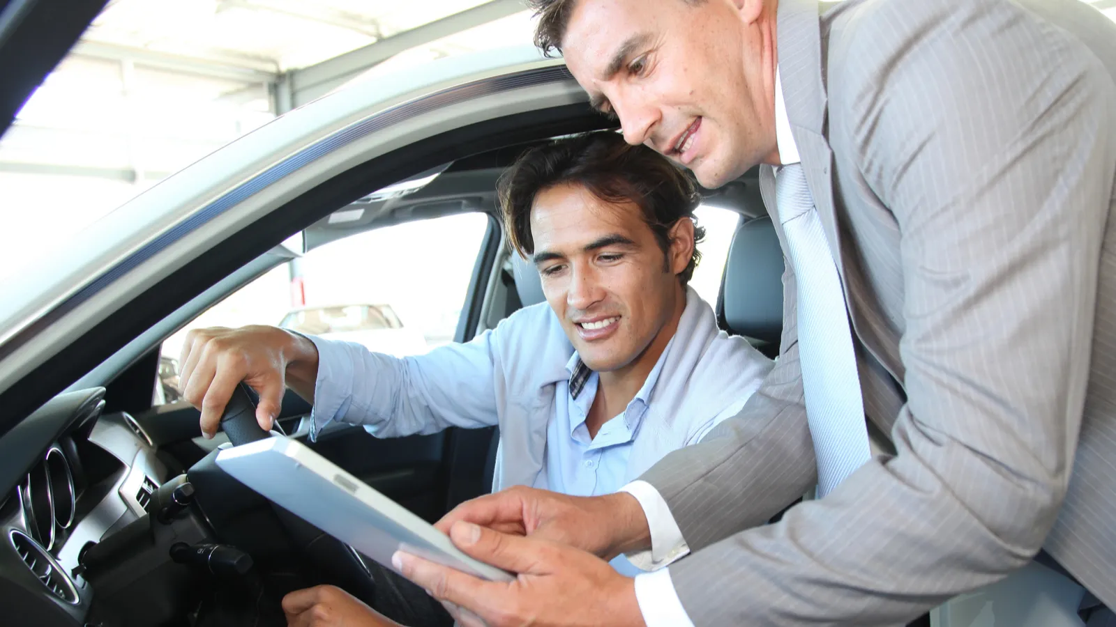 Car seller with car buyer looking-at electronic tablet