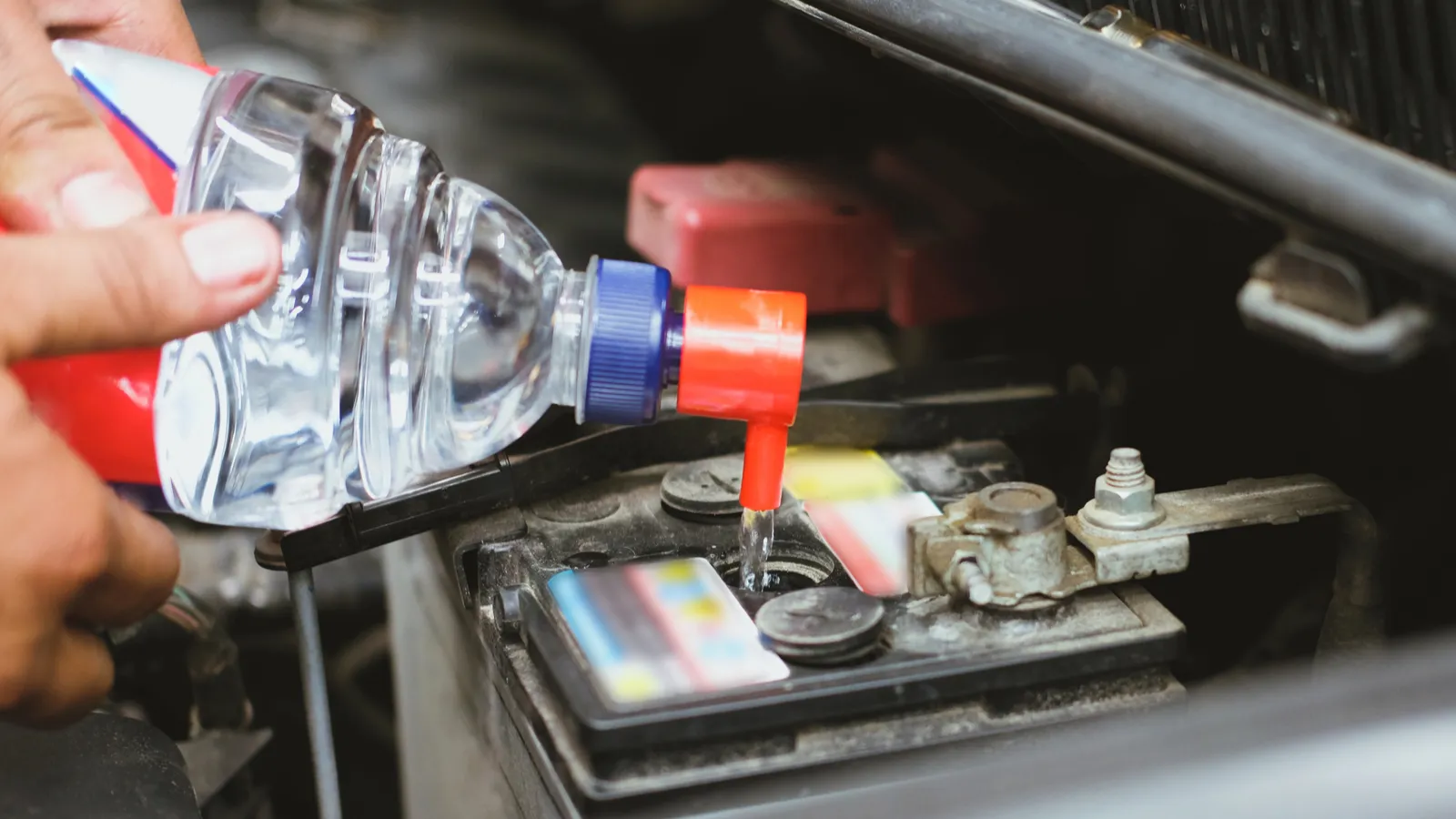 Mechanic pouring distilled water to fill car battery in automobile