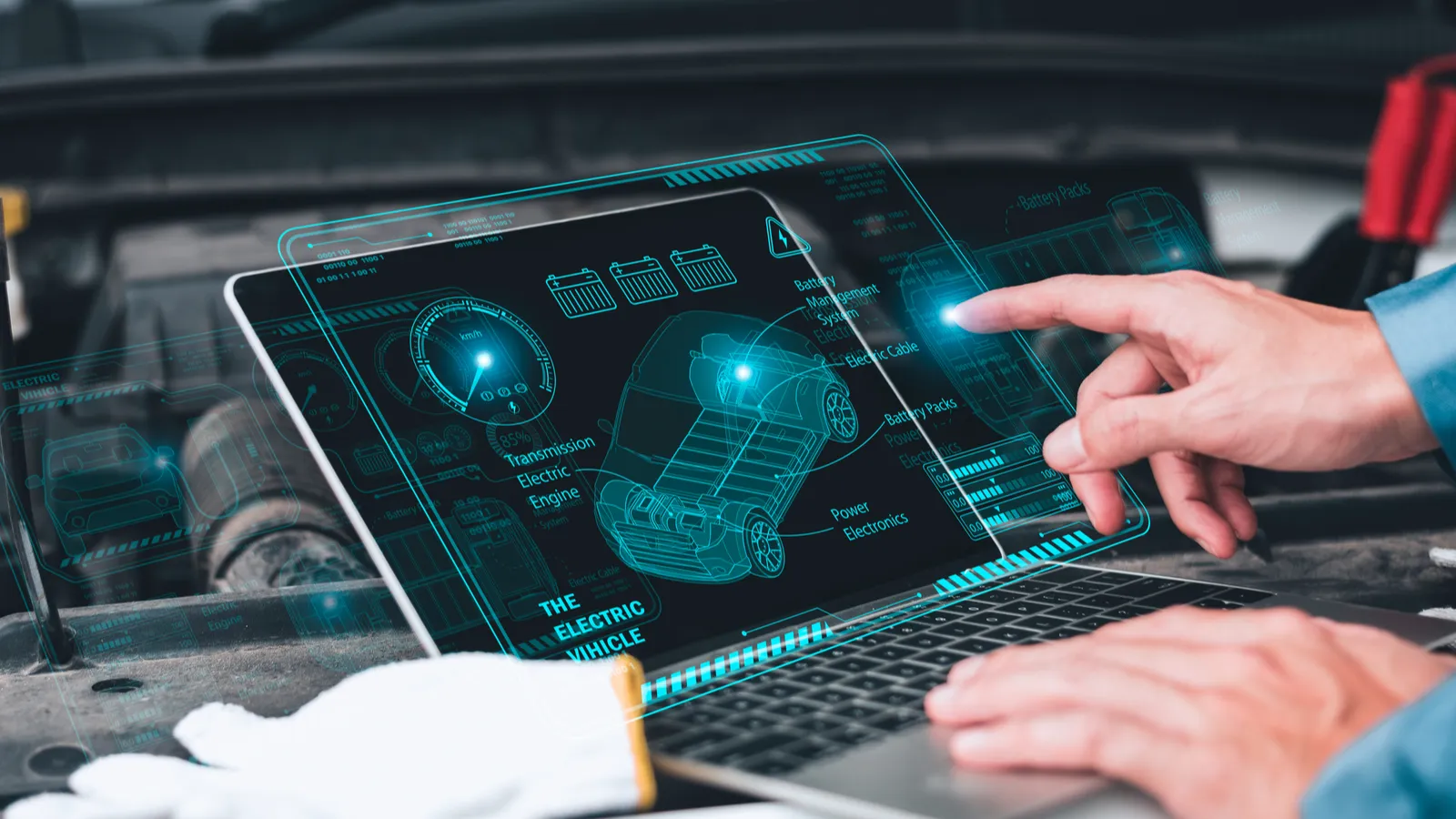 Mechanic working close to an automobile engine while using a laptop