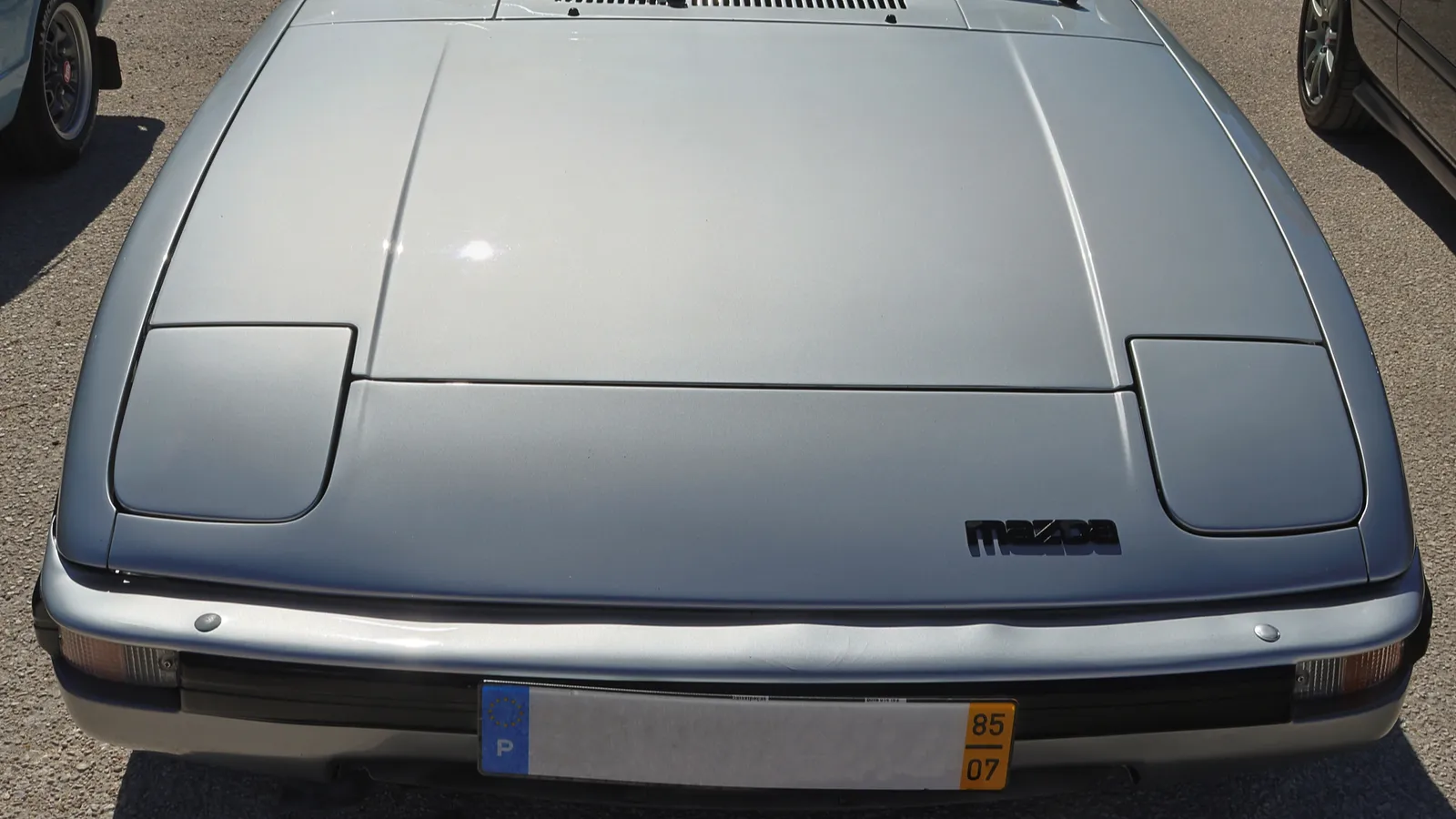 Silver Mazda rx 7 parked in a parking lot reflecting